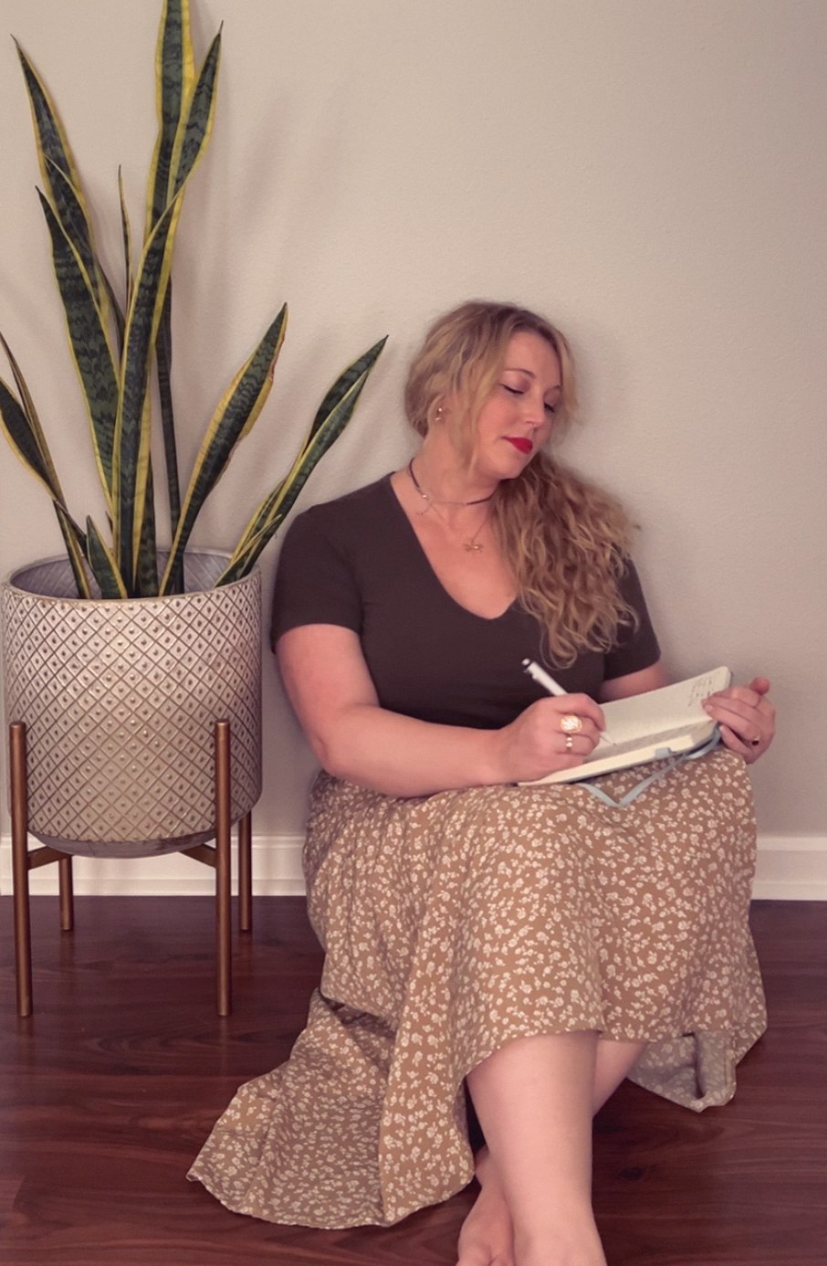 Rebekah journaling at home, seated on the floor beside a snake plant