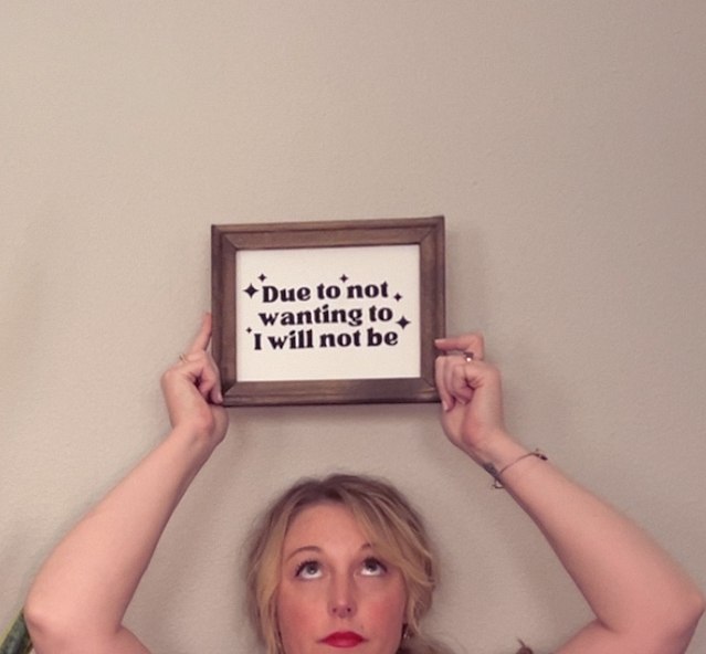 Holding a framed sign reading "Due to not wanting to I will not be"