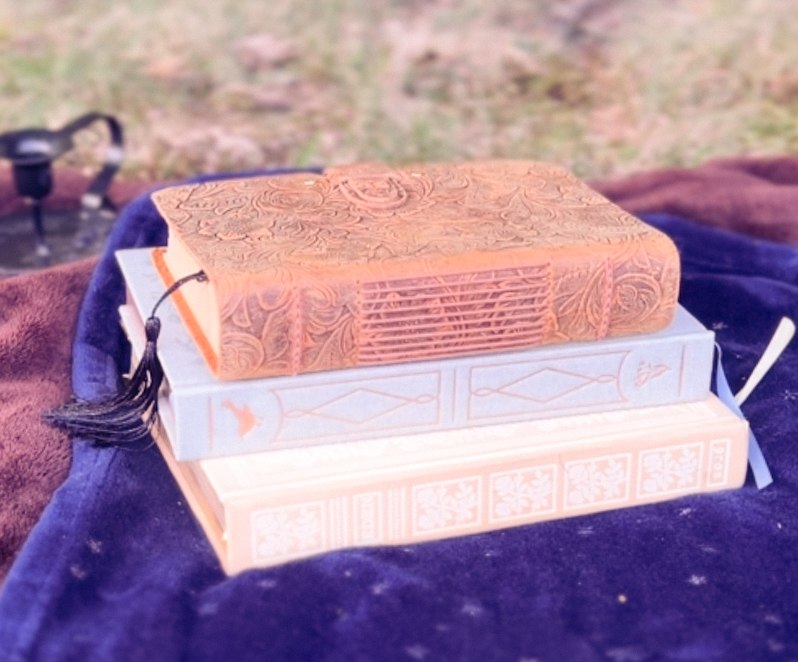 A stack of ornate journals with a tassel bookmark on a starry blue blanket