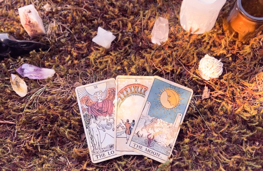 Three tarot cards fanned out on moss, surrounded by crystals and candles